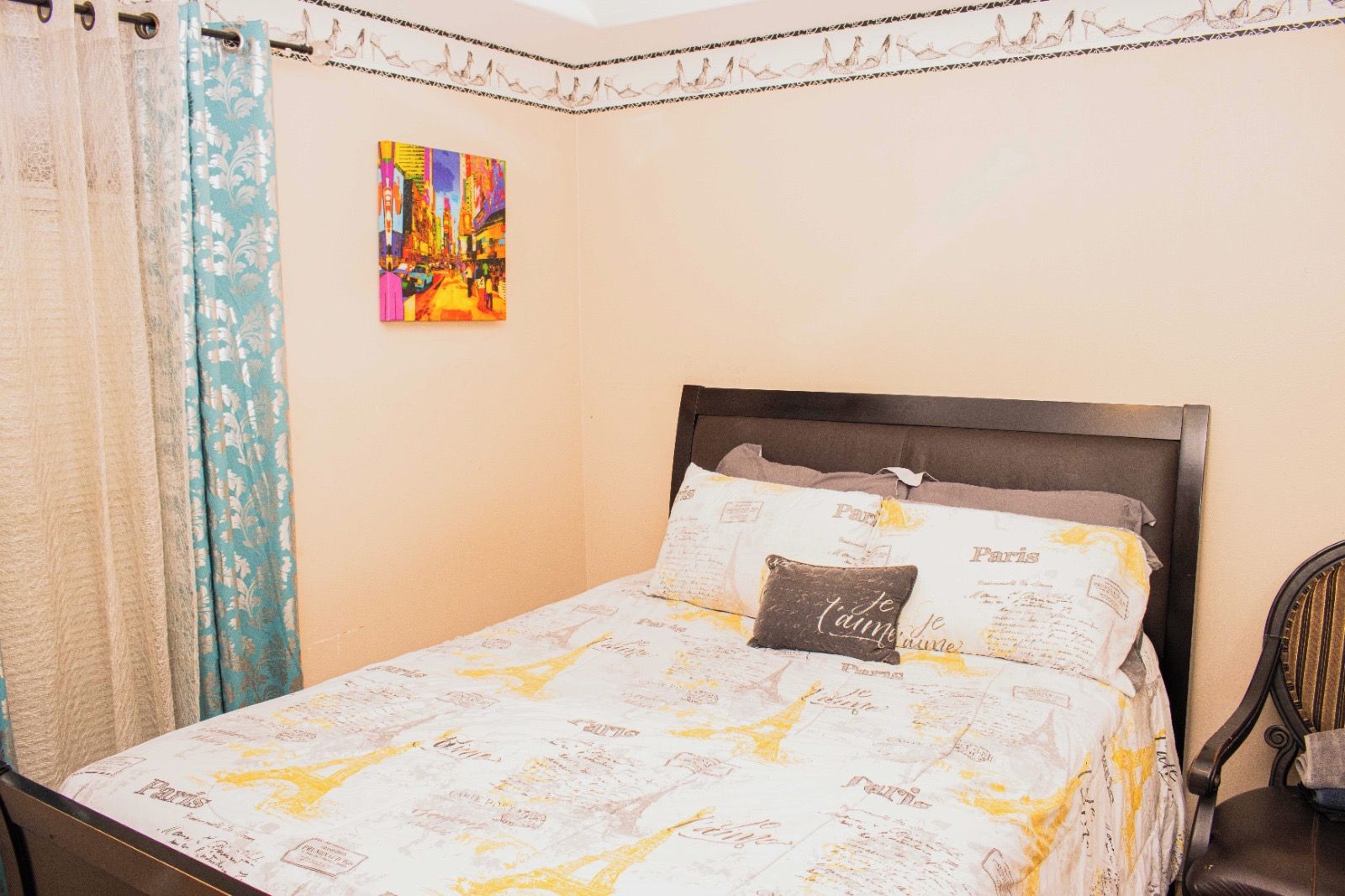 Un lit avec une couvre-lit sur le thème de Paris, un coussin orné du mot « Paris » et un tableau coloré accroché au mur.