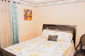 Un lit avec une couvre-lit sur le thème de Paris, un coussin orné du mot « Paris » et un tableau coloré accroché au mur.