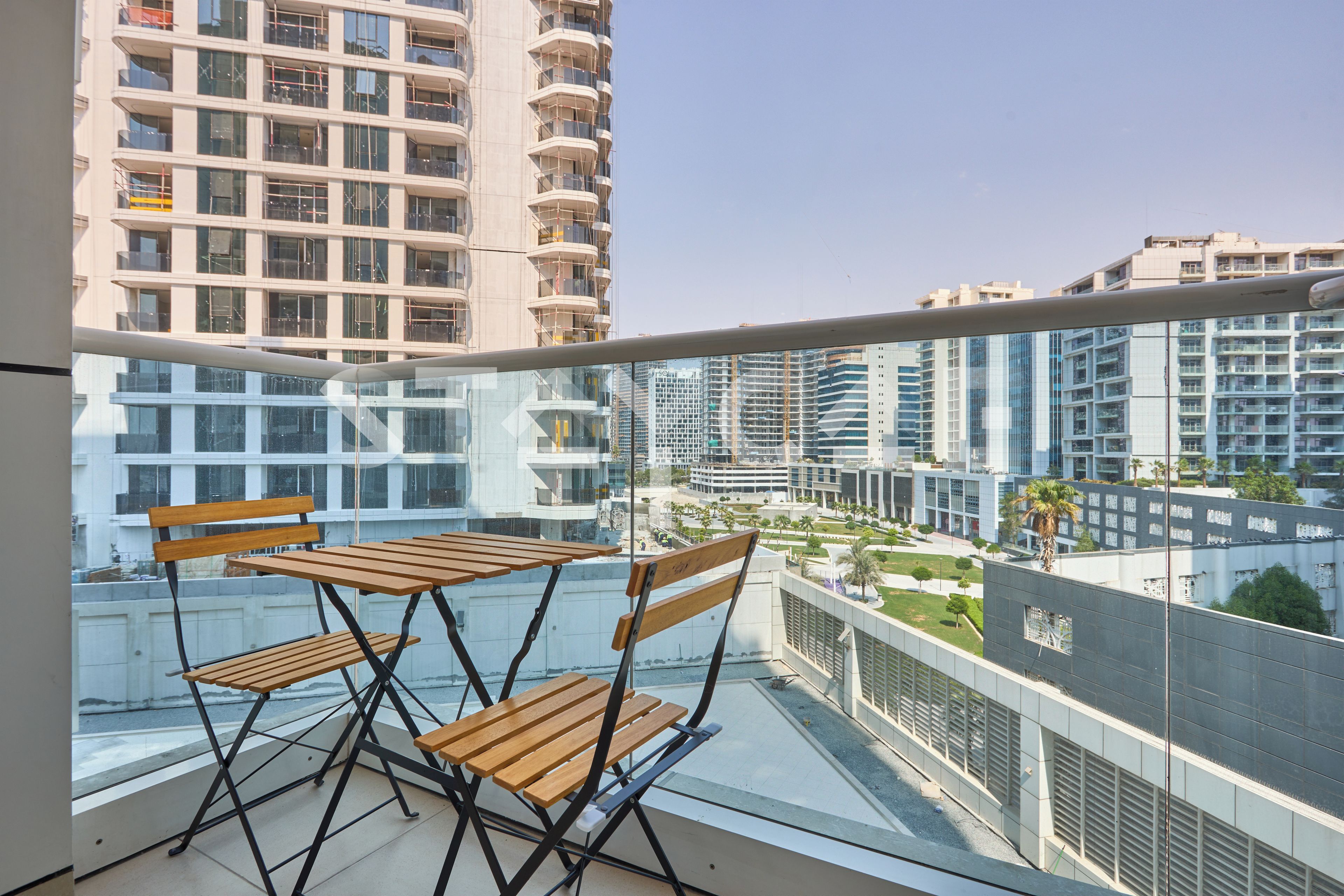 A balcony with two wooden tables and chairs, overlooking a cityscape with modern buildings and a clear sky.