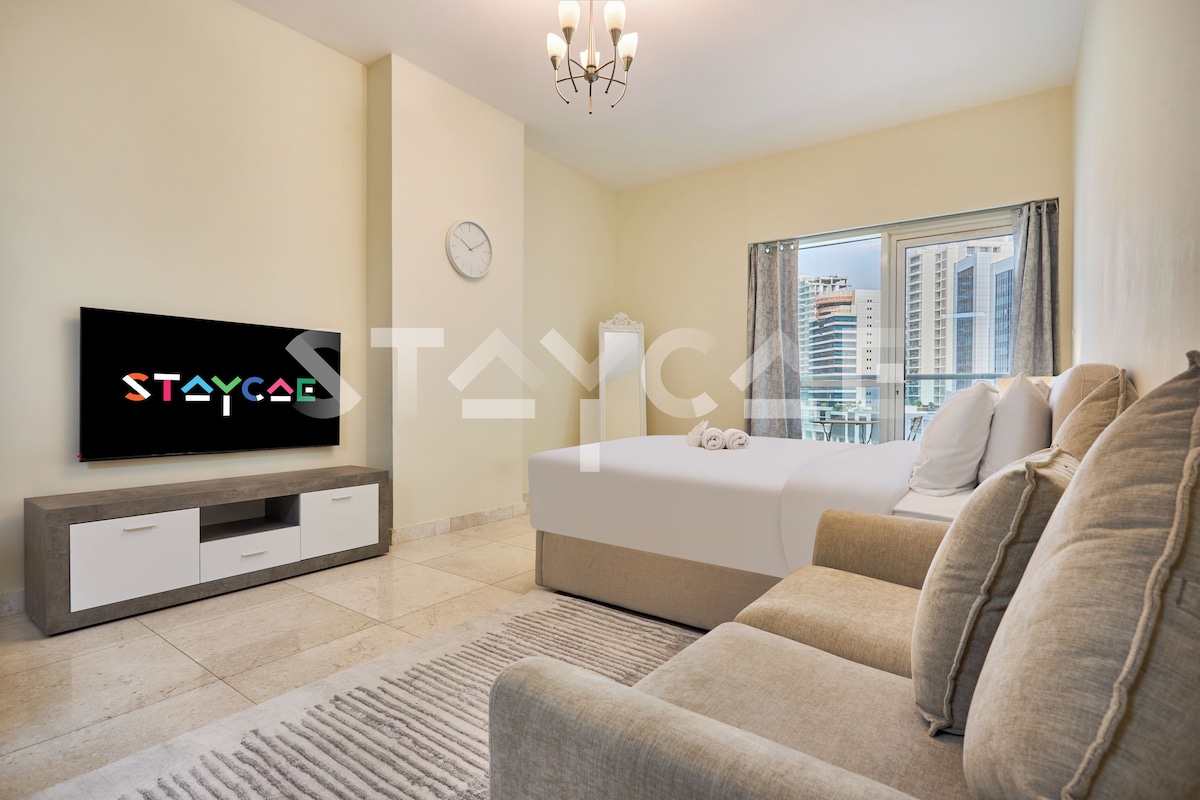 A modern hotel room with a bed, a TV, a sofa, and a view of the cityscape.