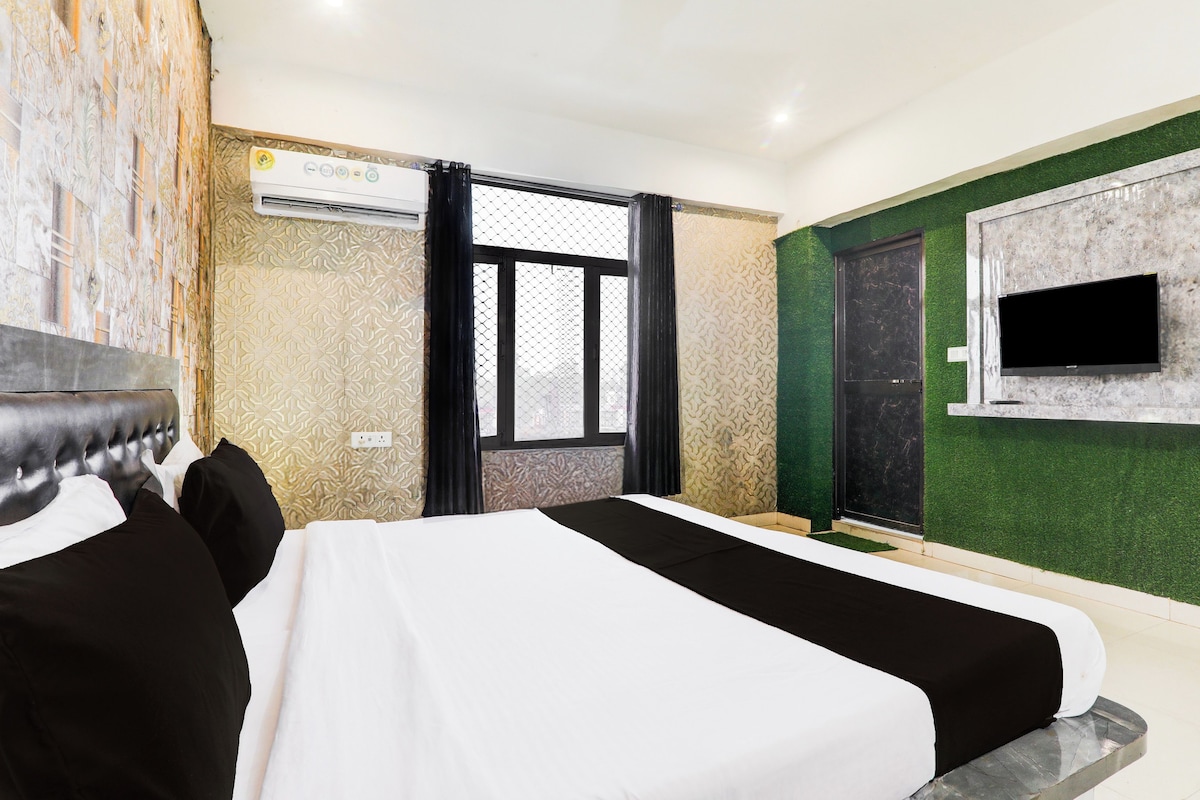 A hotel room with a bed, a TV mounted on the wall, an air conditioning unit, and a window with a view.