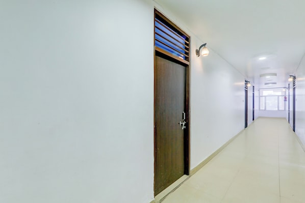 A long, narrow hallway with a wooden door on the left, a light fixture above it, and a window at the end. - Collection O Ayodhya Near Airport (Faizabad)