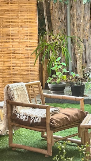Una cadira de fusta amb coixí, una planta en test i una tanca de bambú en un jardí.