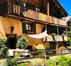 Ein traditionelles Holzhaus mit Balkon, einem Tisch mit Stühlen und Pflanzen im Vordergrund.