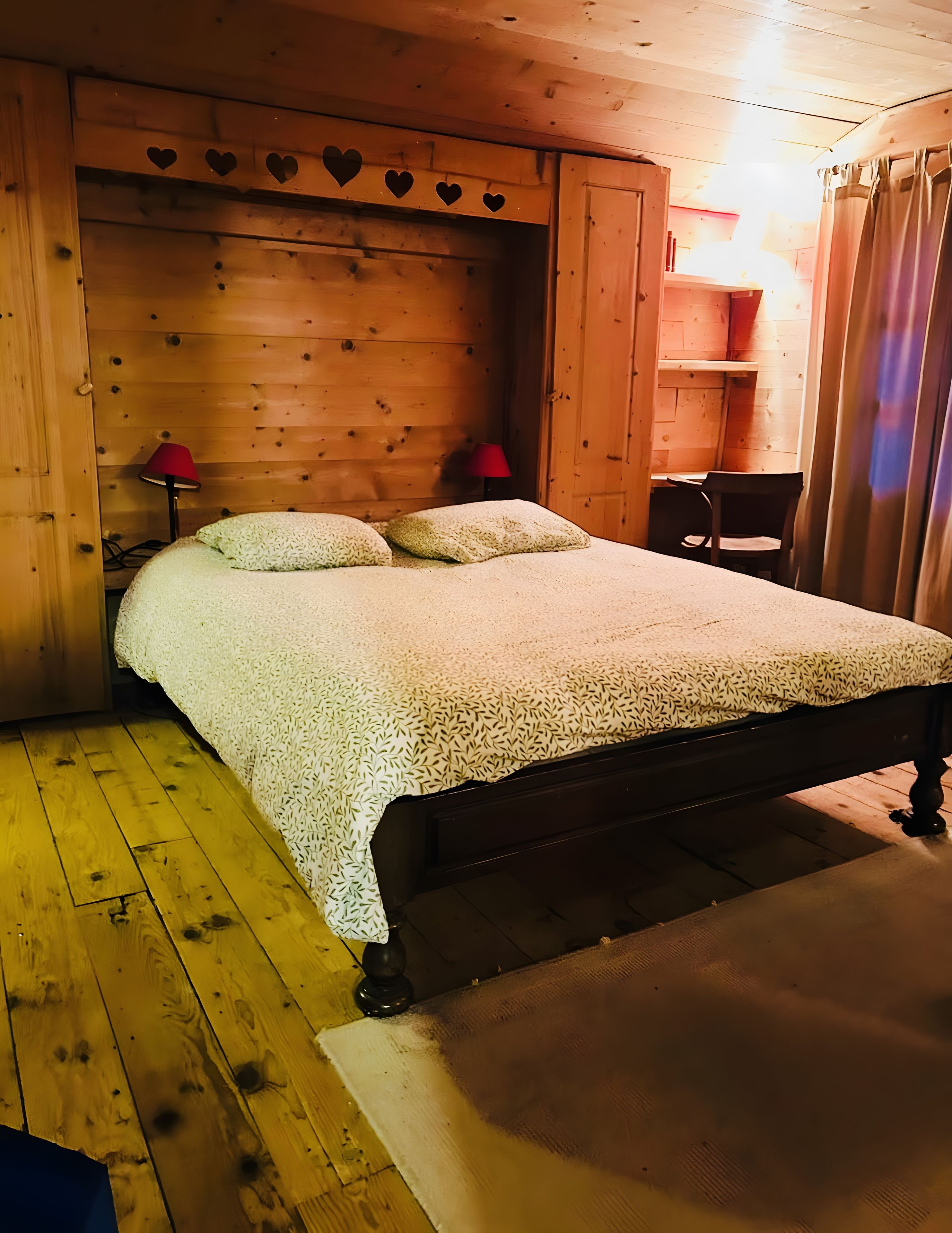 A wooden room with a bed, a nightstand, a lamp, and a small table.