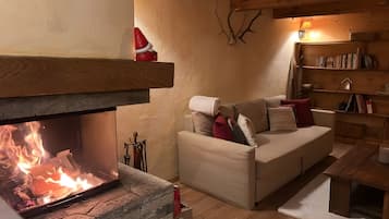 Una sala de estar acogedora con chimenea, un sofá con cojines, una estantería de madera y un revestimiento de piedra alrededor de la chimenea.