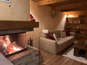 Una sala de estar acogedora con chimenea, un sofá con cojines, una estantería de madera y un revestimiento de piedra alrededor de la chimenea.