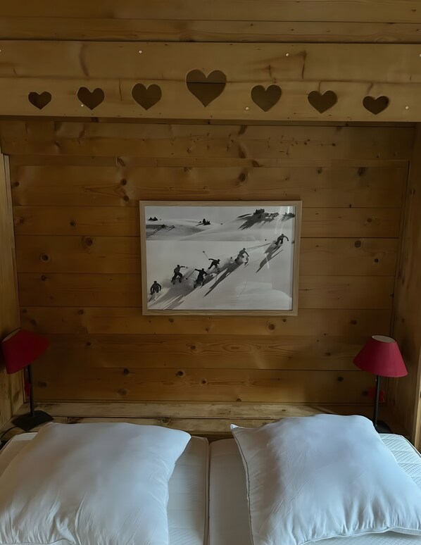 Interior de una cabaña de madera con una fotografía enmarco de esquiadores en una ladera, dos almohadas y una lámpara roja.