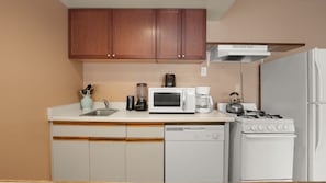 Cocina compacta con armarios de madera, microondas, cafetera, hervidor y lavavajillas.