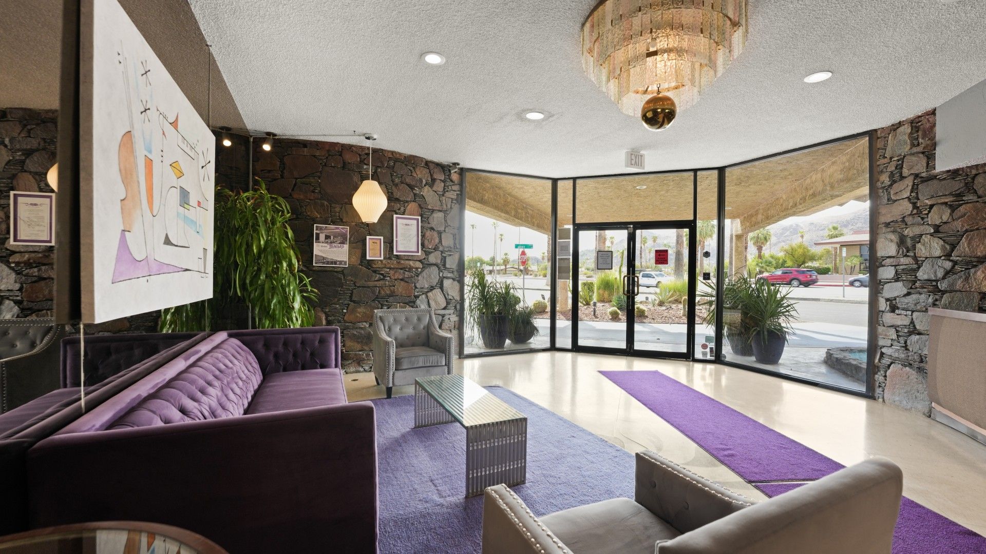 A lobby with a stone wall, a purple sofa, a chandelier, and a view of the outside.
