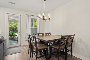 A dining area with a wooden table and chairs, a chandelier, and a view of greenery outside. - New on Program! Ready to Rent in The Townes at Barefoot #5206! Perfect Spot! (North Myrtle Beach)