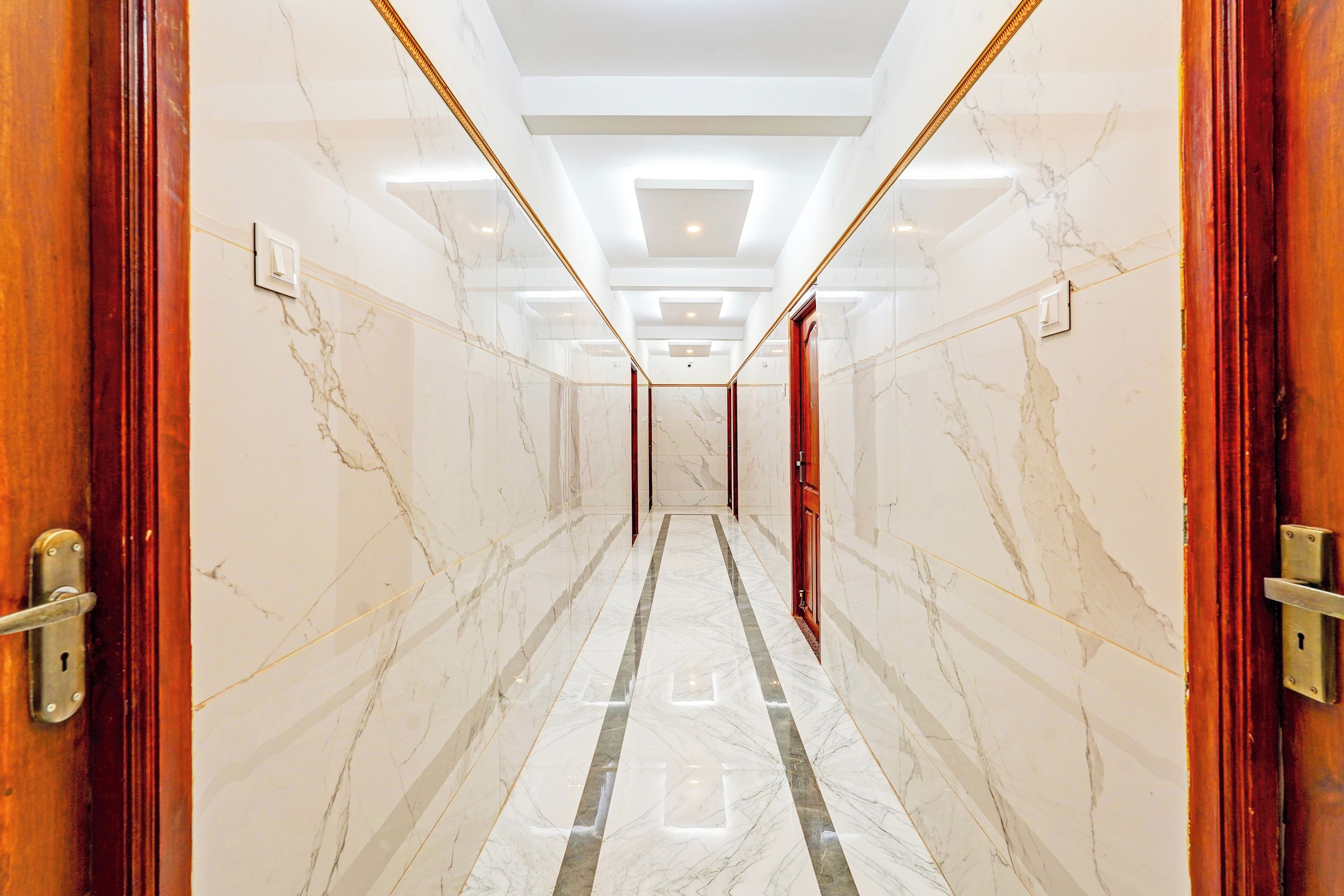 A hallway with marble walls and a reflective floor, leading to a room with a door.