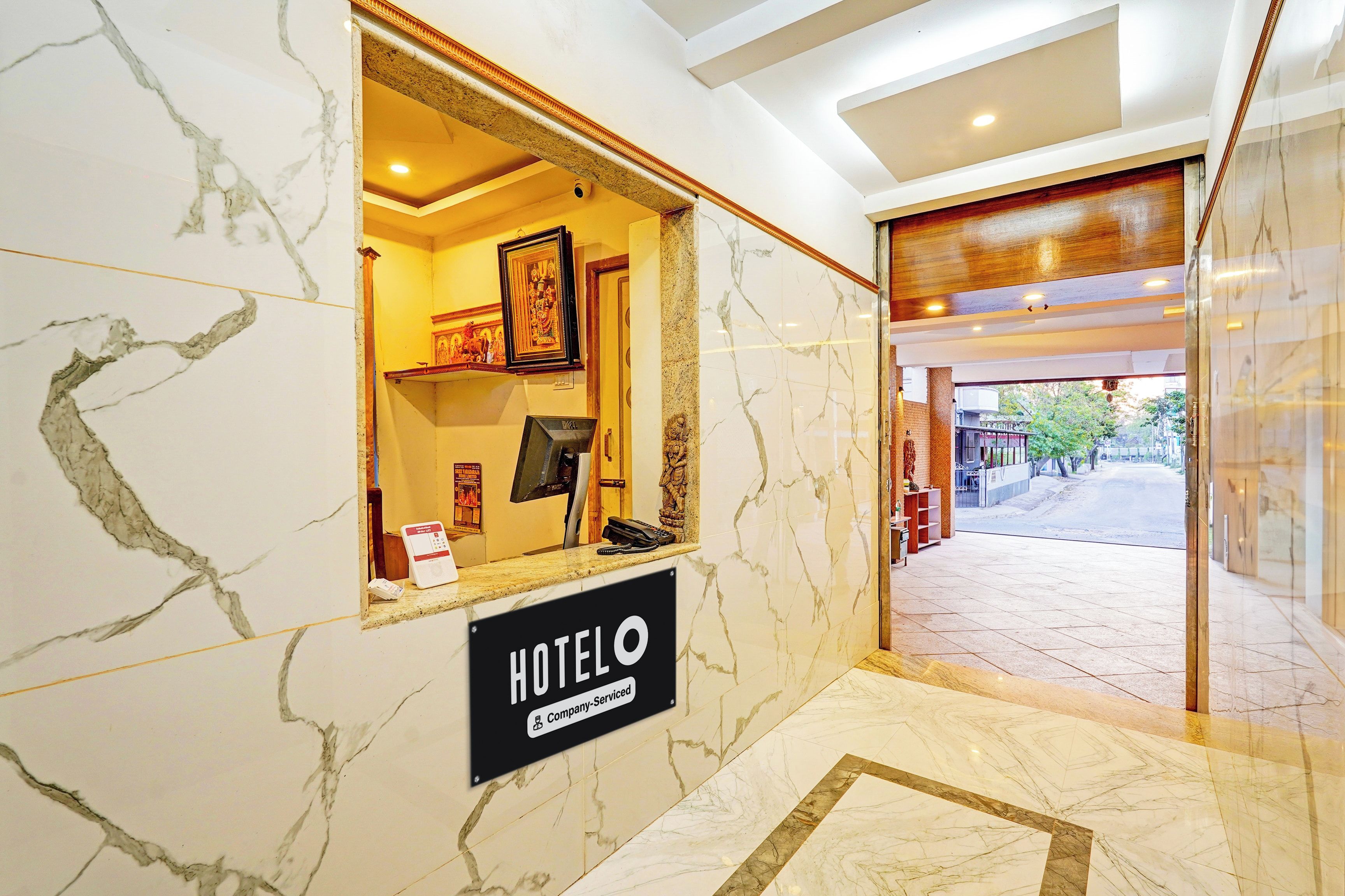 Zona de recepción de un hotel con piso de mármol, un mostrador de recepción, un cuadro enmarcado sobre el mostrador y un cartel que indica que el hotel cuenta con servicios para empresas.