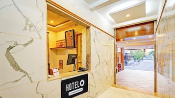 Zona de recepción de un hotel con piso de mármol, un mostrador de recepción, un cuadro enmarcado sobre el mostrador y un cartel que indica que el hotel cuenta con servicios para empresas.