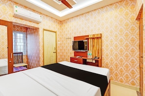 A hotel room with a bed, a desk with a mirror, a television, and an air conditioning unit.