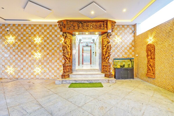 A hotel lobby with a checkered floor pattern, a central staircase, and a decorative wooden archway.