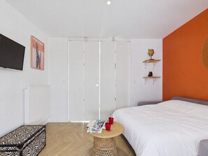 A bedroom with a bed, a small round table with magazines and red cups, a zebra-patterned suitcase, a white radiator, a TV on the wall, and a sliding door closet. - 15-person house, heated pool, near beach (Saint-Alban)