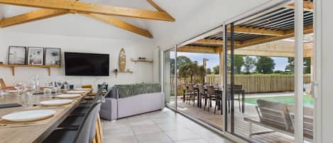 A modern kitchen with a long dining table, a built-in oven, and a large window overlooking a deck.