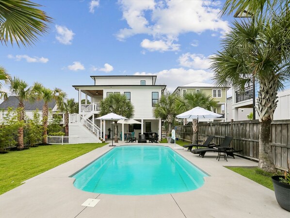 Un jardin avec une piscine, une terrasse couverte et une clôture en bois.