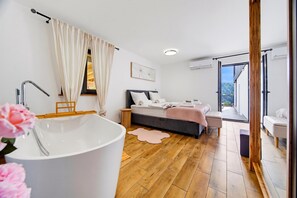 Ein modernes Schlafzimmer mit einer großen Badewanne, einem Bett mit rosa Decke und Blick auf einen Balkon.