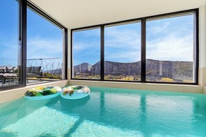 A pool with clear water, two floating rings, and a view of mountains through large windows. - Forest Peak Retreat With Indoor Pool and Sauna (Ravna Gora)