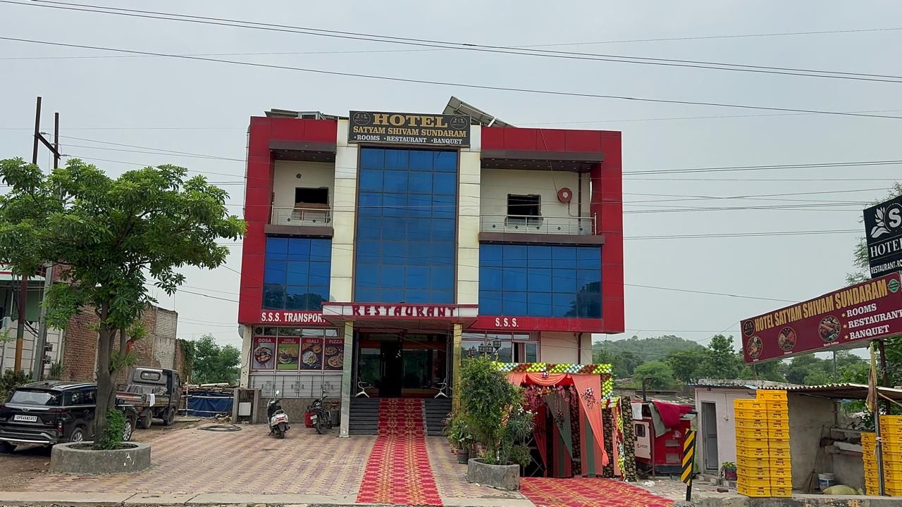 A hotel with a red and blue facade, a visible entrance, and a sign indicating it offers rooms, a restaurant, and a banquet.