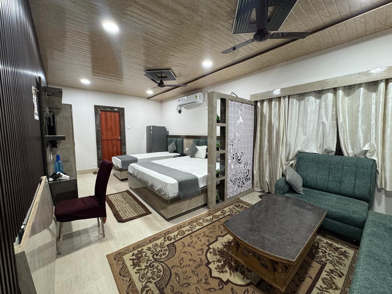 A hotel room with a bed, a sofa, a chair, a coffee table, and a decorative partition.