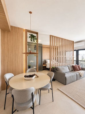 A modern living room with a round dining table, grey sofas, and a wooden partition. - SETIN 2207 (São Paulo)
