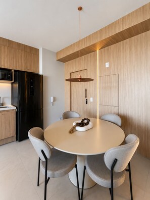 A modern kitchen with a round dining table, grey upholstered chairs, a hanging pendant light, and a black refrigerator. - SETIN 2207 (São Paulo)