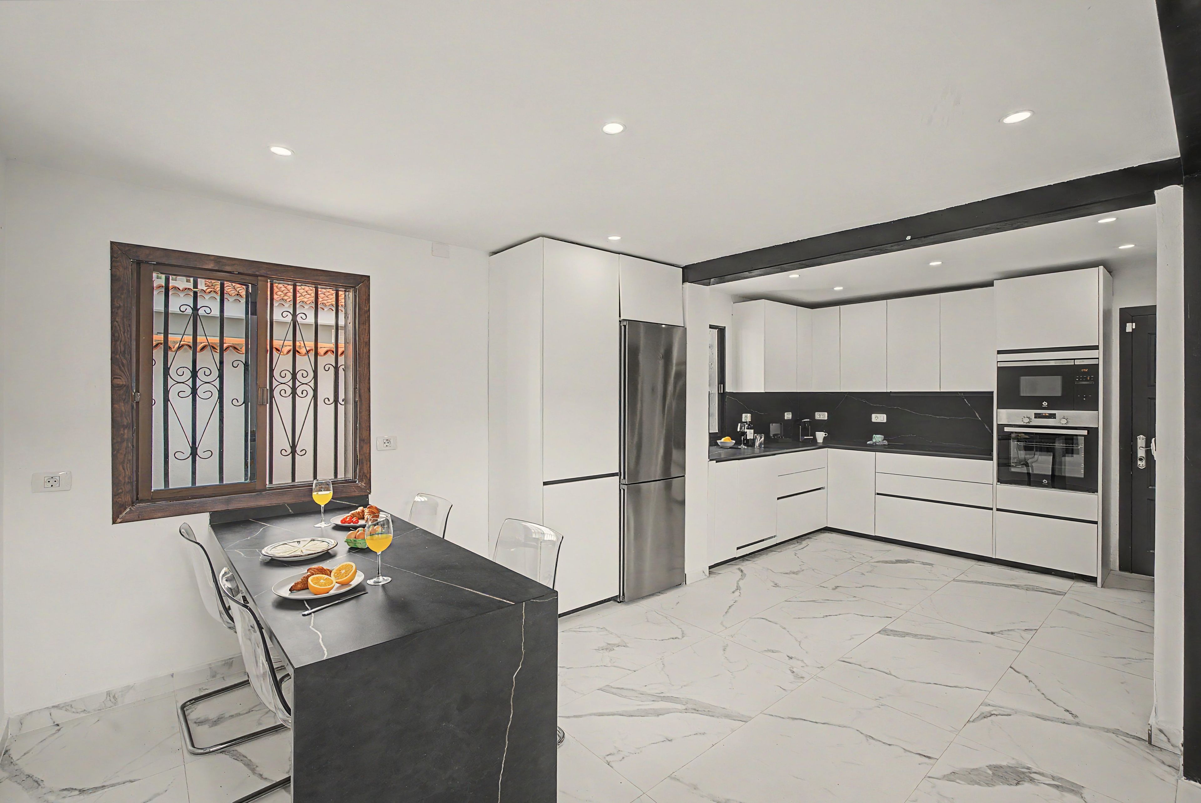Una cocina moderna con armarios blancos, un refrigerador de acero inoxidable y una encimera negra.