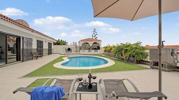 Zona junto a la piscina con piscina, sillas de descanso y una mesa con bebidas.