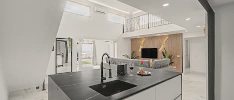 A modern kitchen with a central island, a dining area with a sofa, and a TV mounted on the wall.