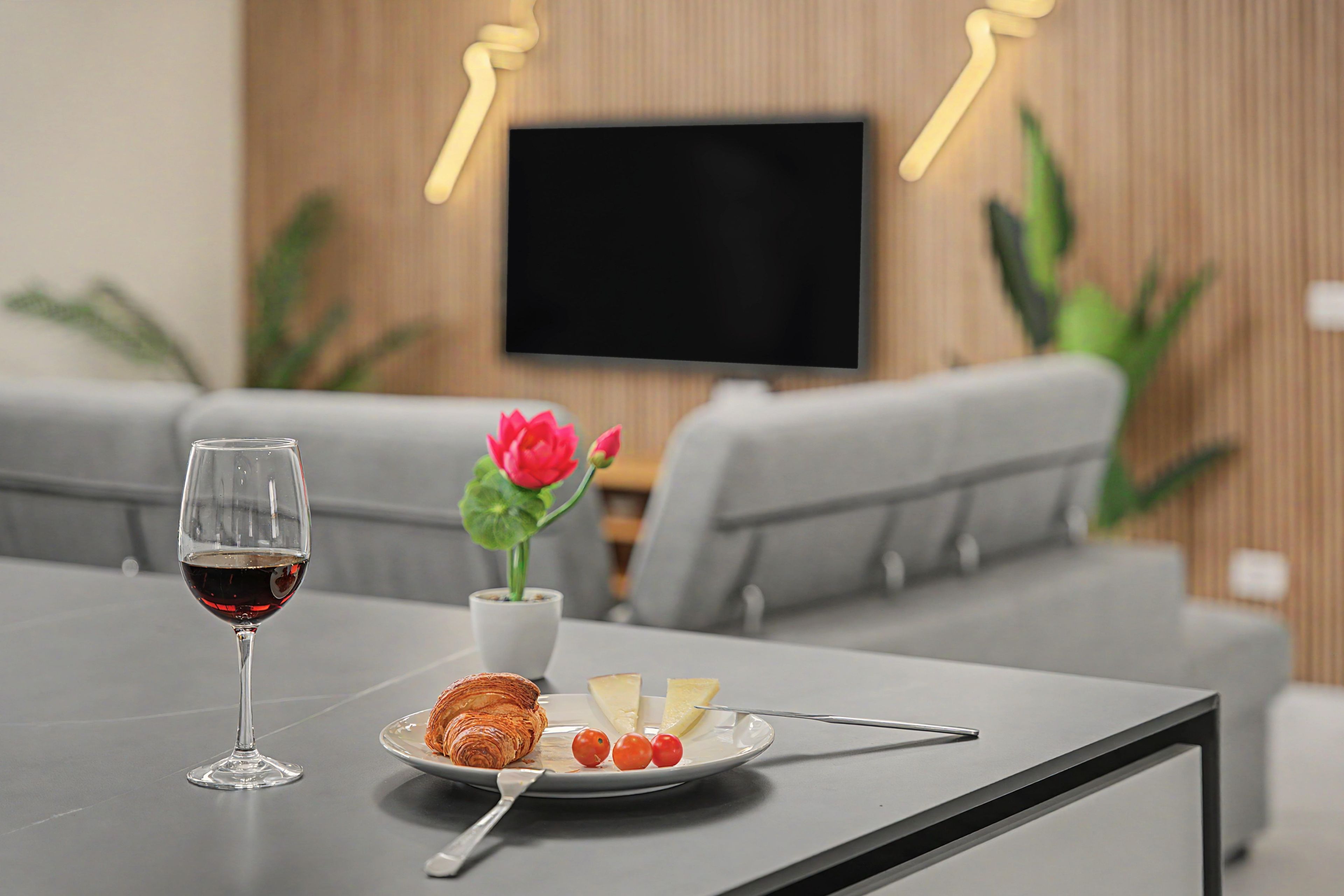 Una mesa de comedor con una copa de vino, un plato con un croissant, queso y tomates, y un florero.