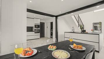 Un comedor moderno con una mesa de mármol negro, una cocina al fondo y una escalera que sube a otro nivel.