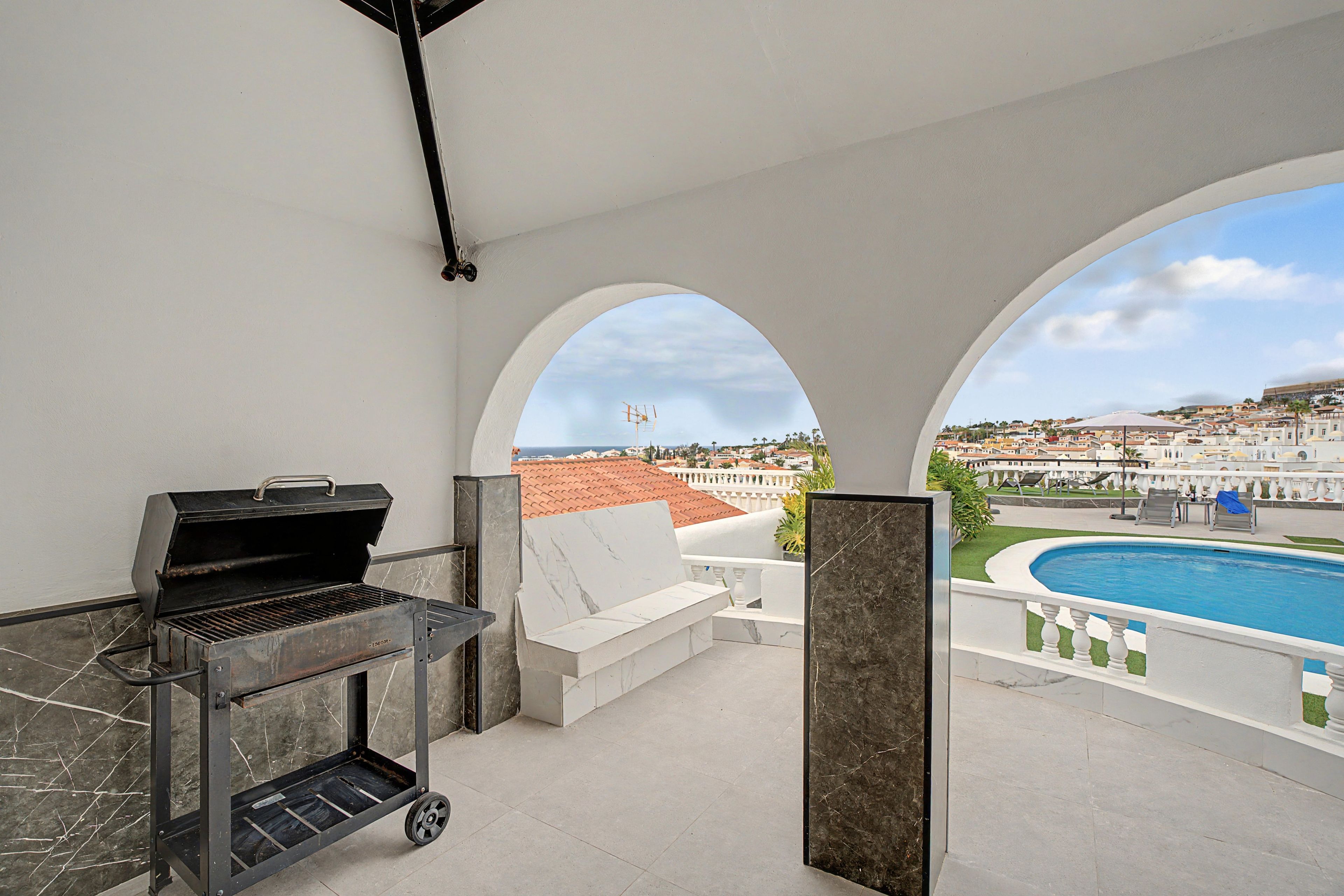 En balkon med grill, pool og udsigt over en by.