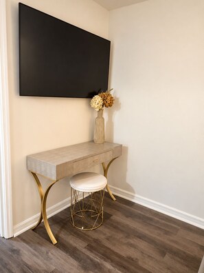 Un intérieur moderne avec un téléviseur à écran plat fixé au mur, une console de couleur claire agrémentée d’un vase de fleurs et un tabouret aux pieds dorés.