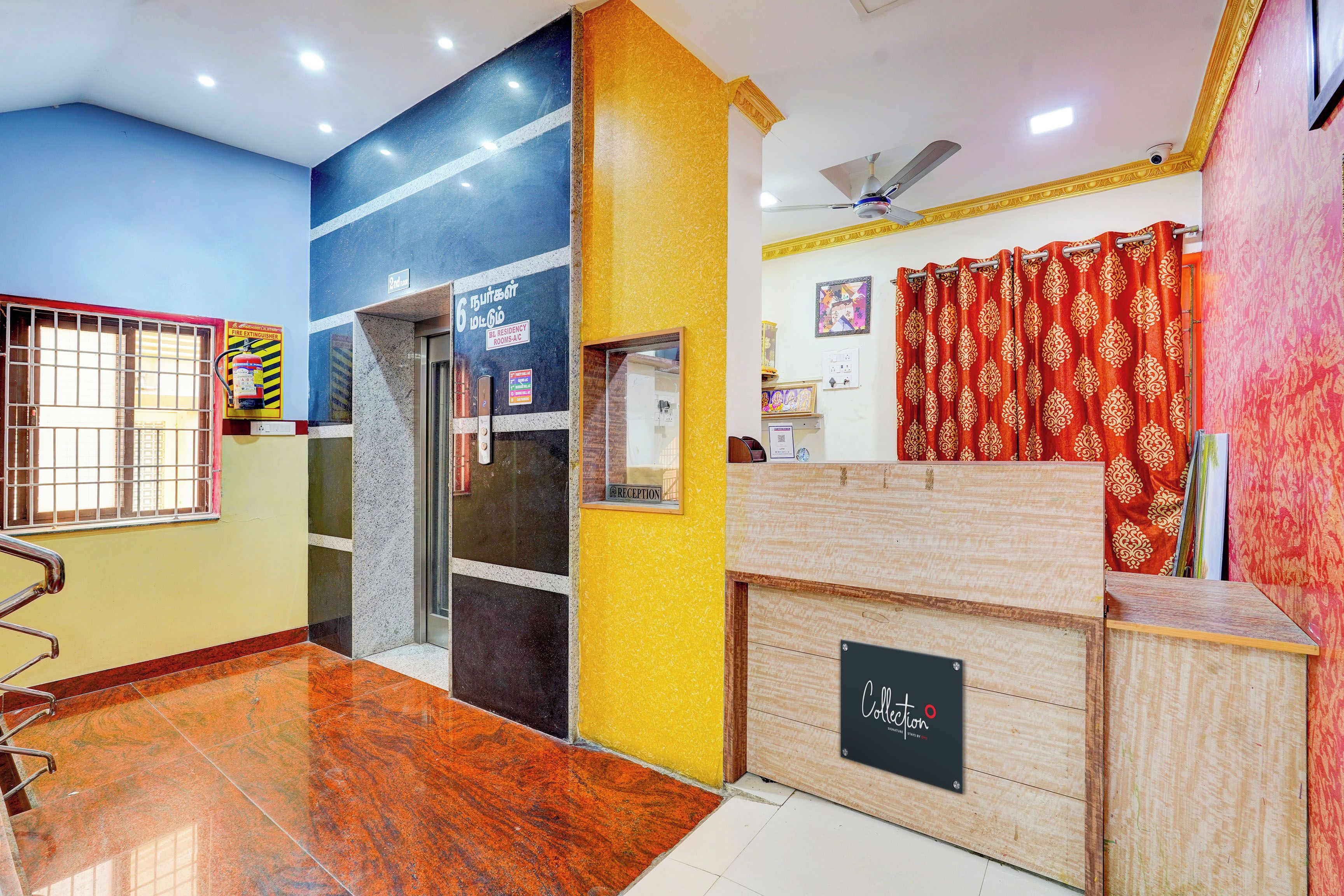 A reception area with a reception desk, a fire extinguisher, and a sign indicating room numbers.