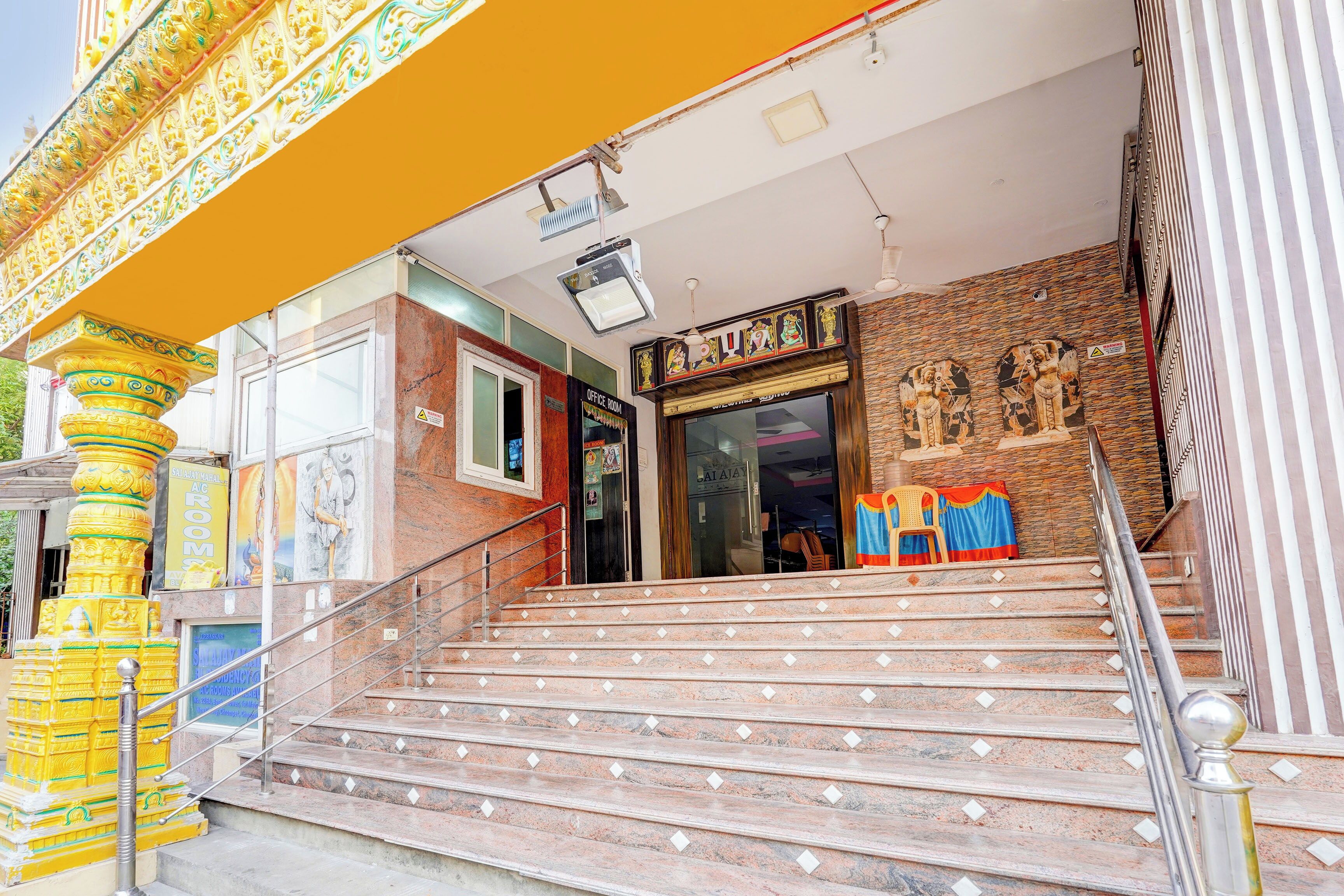 Una escalera conduce a una sala de oficina con un letrero de advertencia, una pared de piedra con estatuas y un pilar amarillo con detalles intrincados.