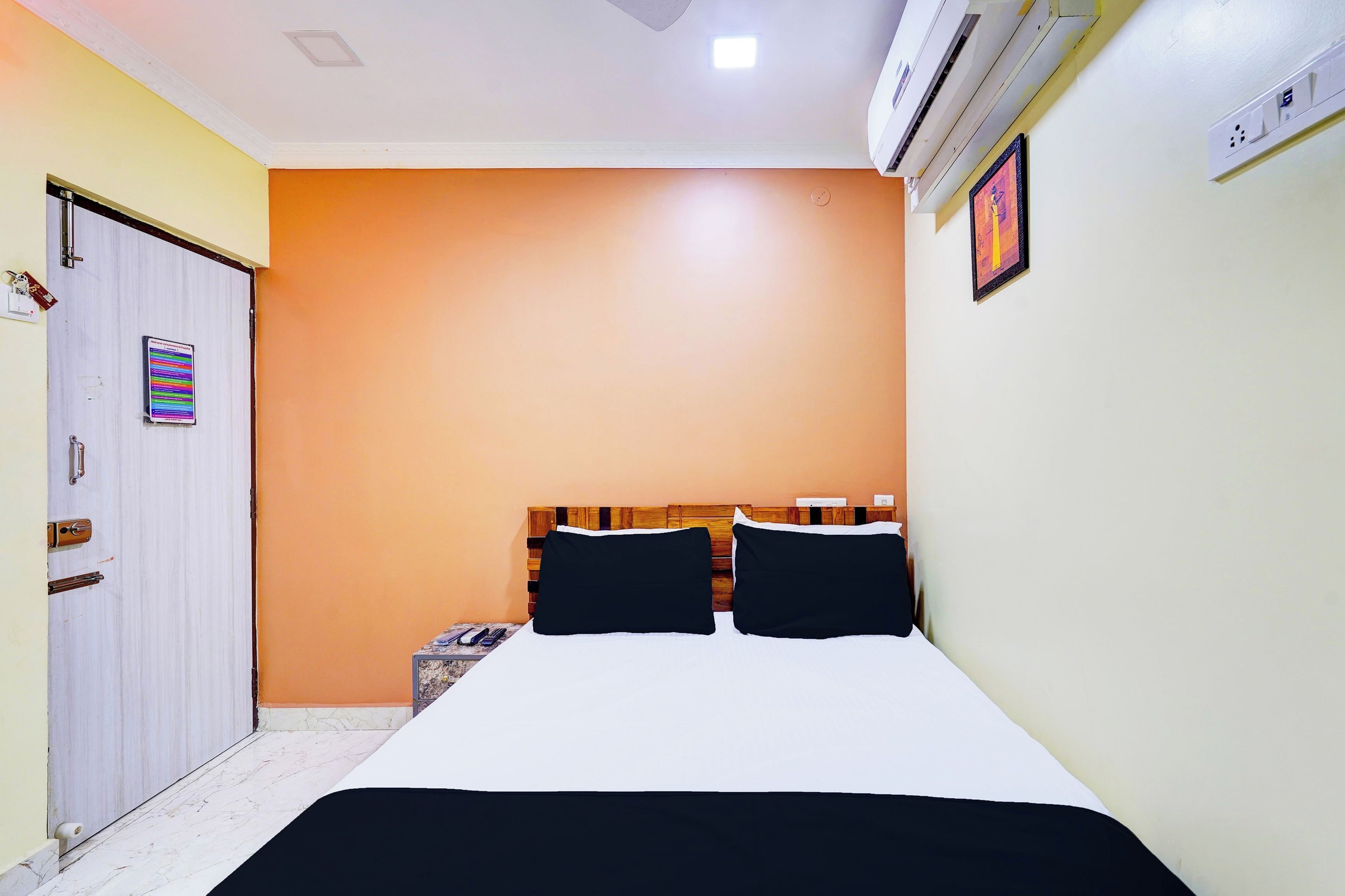 A bedroom with a bed, a wardrobe, an air conditioning unit, and a wall-mounted picture.
