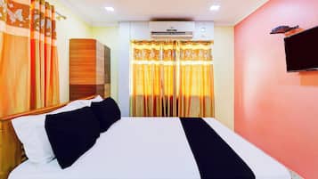 Una habitación de hotel con cama, cortinas, unidad de aire acondicionado y televisor en la pared.