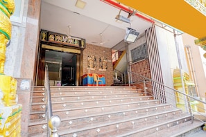 A temple entrance with steps leading up to a door, a statue, and a signboard.