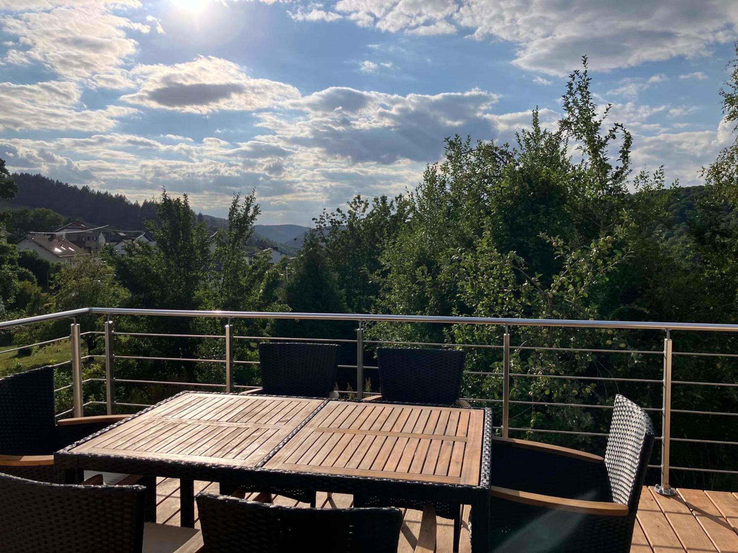 Eine Terrassengruppe im Freien mit einem Holztisch und Korbstühlen, umgeben von einem Metallgeländer.