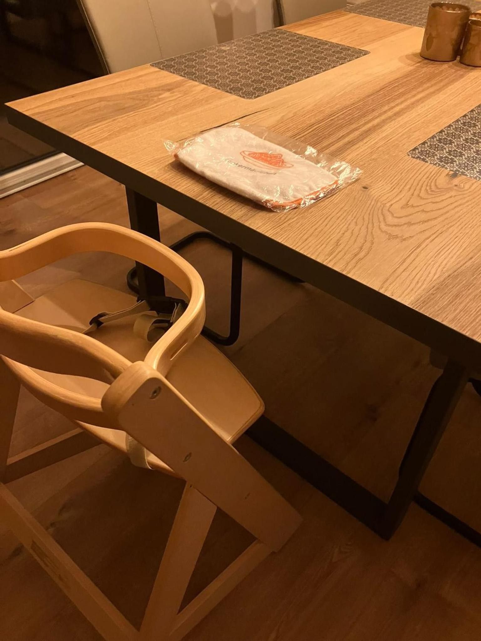 A wooden table with a plastic bag on it, a chair with a headrest, and a patterned rug on the floor.