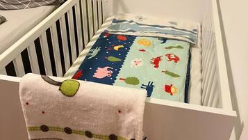 A white crib with a colorful blanket and a pillow.