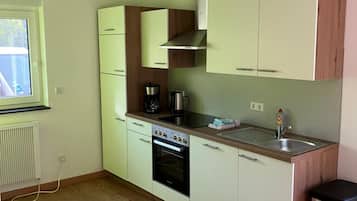 Eine kleine Küche mit weißen Schränken, einem eingebauten Backofen, einer Kaffeemaschine und einem Fenster.