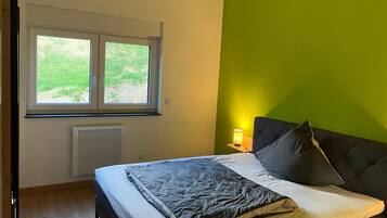 Un dormitorio con cama, ventana, radiador y pared verde.