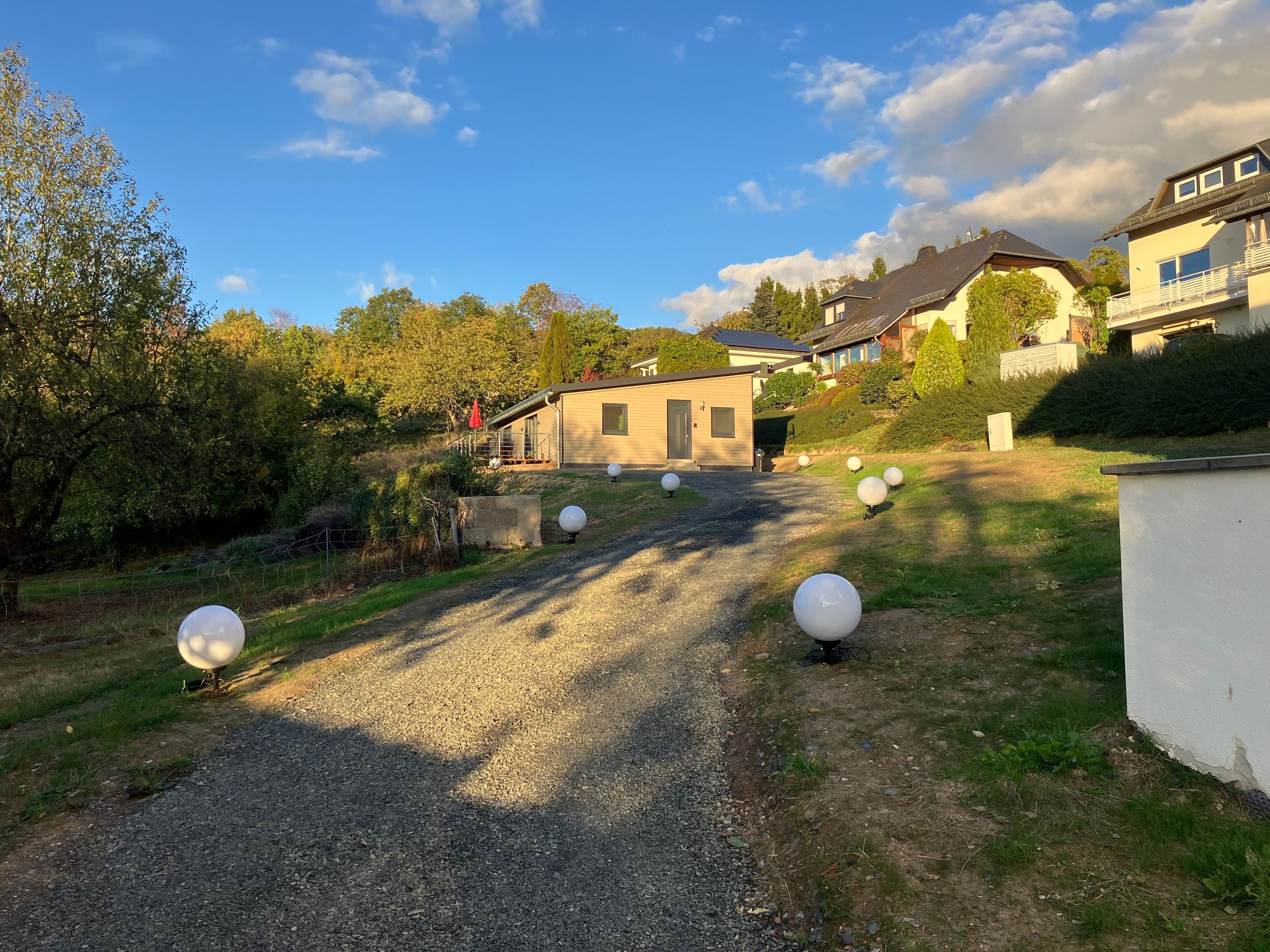 A gravel driveway leading to a house with a small porch and a red umbrella.
