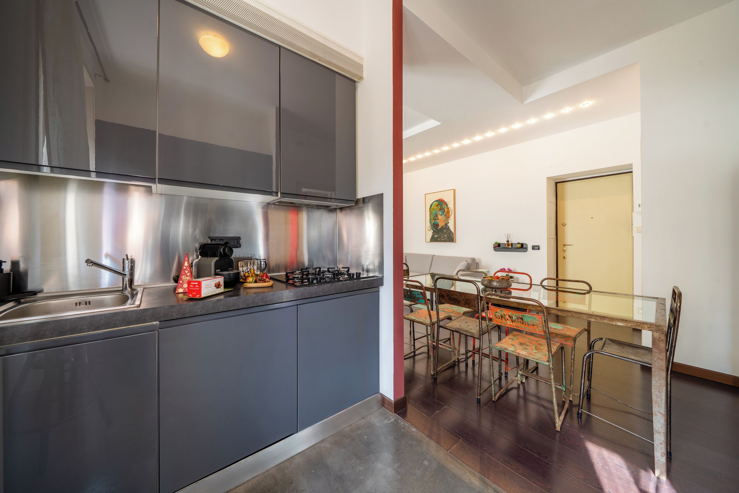 Una cucina moderna con elettrodomestici in acciaio inossidabile, un'area pranzo con sedie diverse e un quadro appeso al muro.