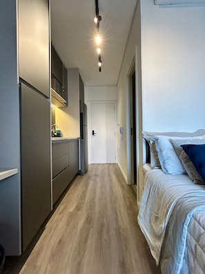 A narrow hallway leading to a bedroom with a bed, a kitchenette, and a door at the end. - SETIN 2302 (São Paulo)