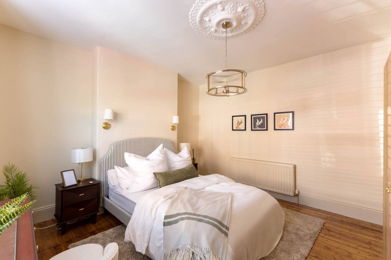 A bedroom with a bed, bedside lamps, a radiator, and framed pictures on the wall.